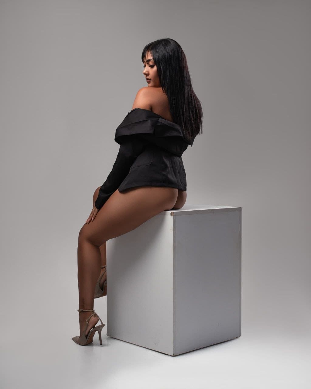 Cielo, escort está sentada de perfil sobre un cubo blanco minimalista en Malaga-153