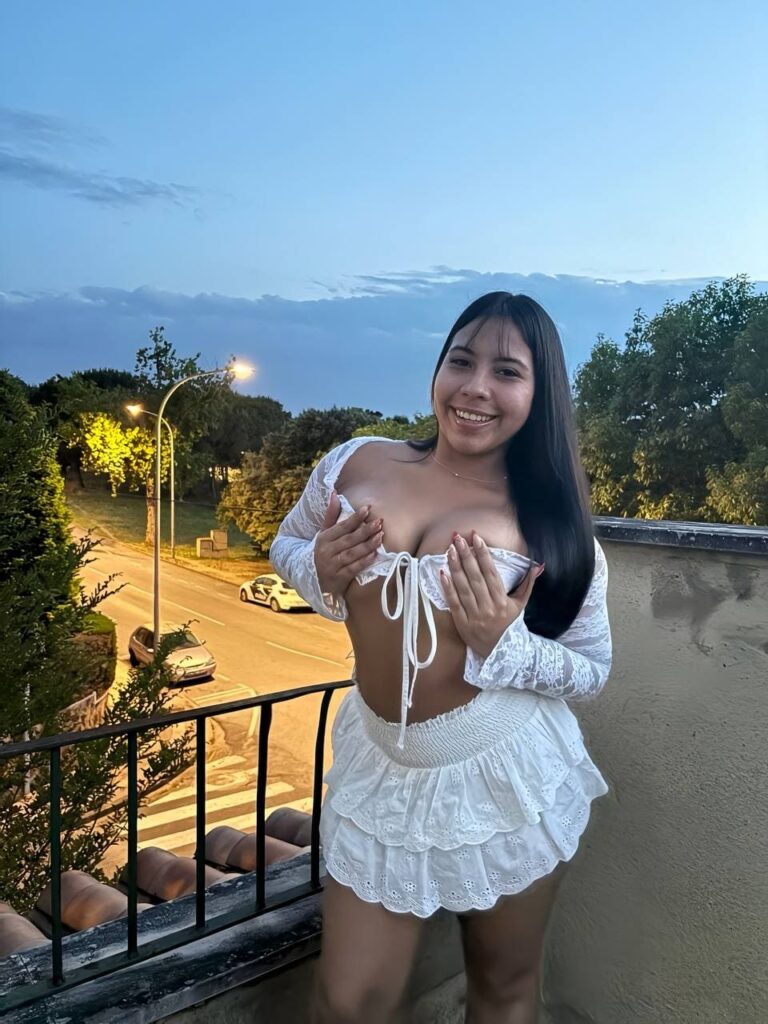 Nathy, escort posa sonriendo mientras sostiene su top blanco en Malaga