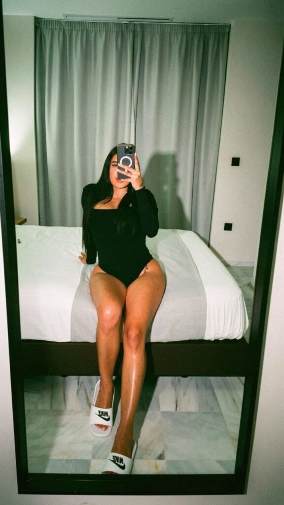 Evelyn, escort está sentada en el borde de una cama con sábanas blancas en Malaga